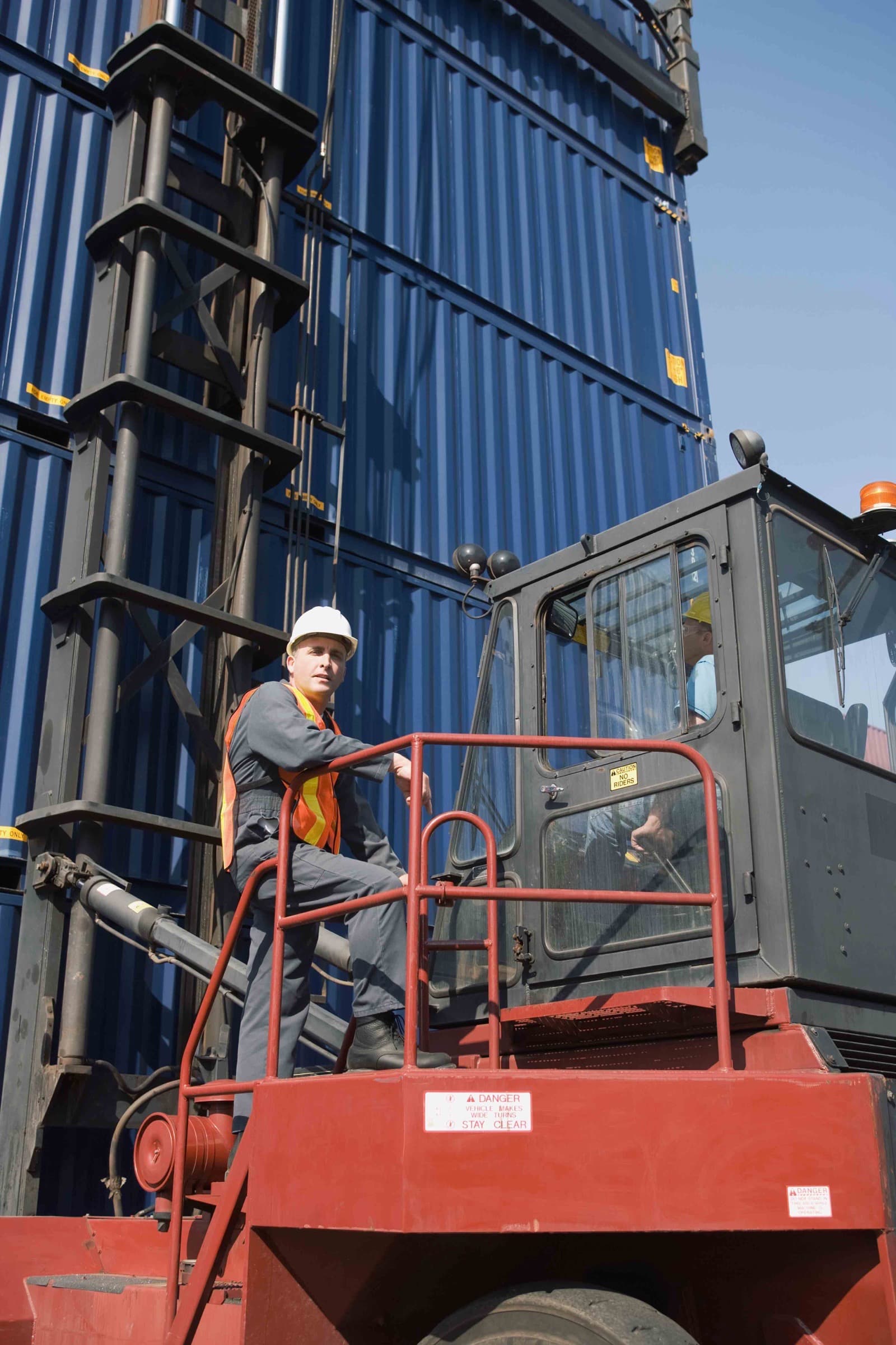 A worker on a lift platform beside stacked shipping containers