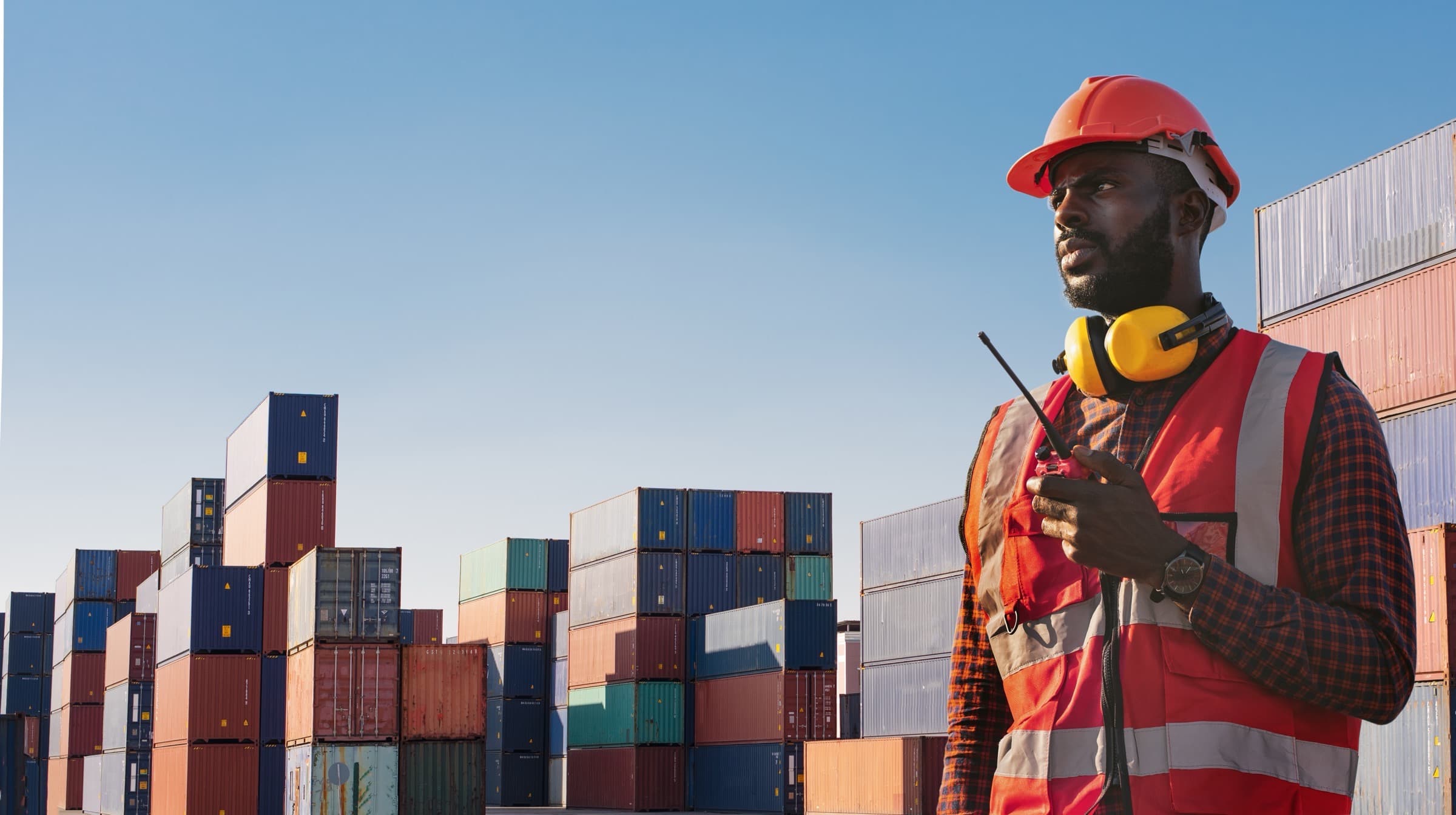A longshoreman with a radio in front of stacked containers